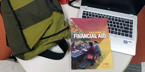Table with Your Guide To Financial Aid book, laptop and backpack.